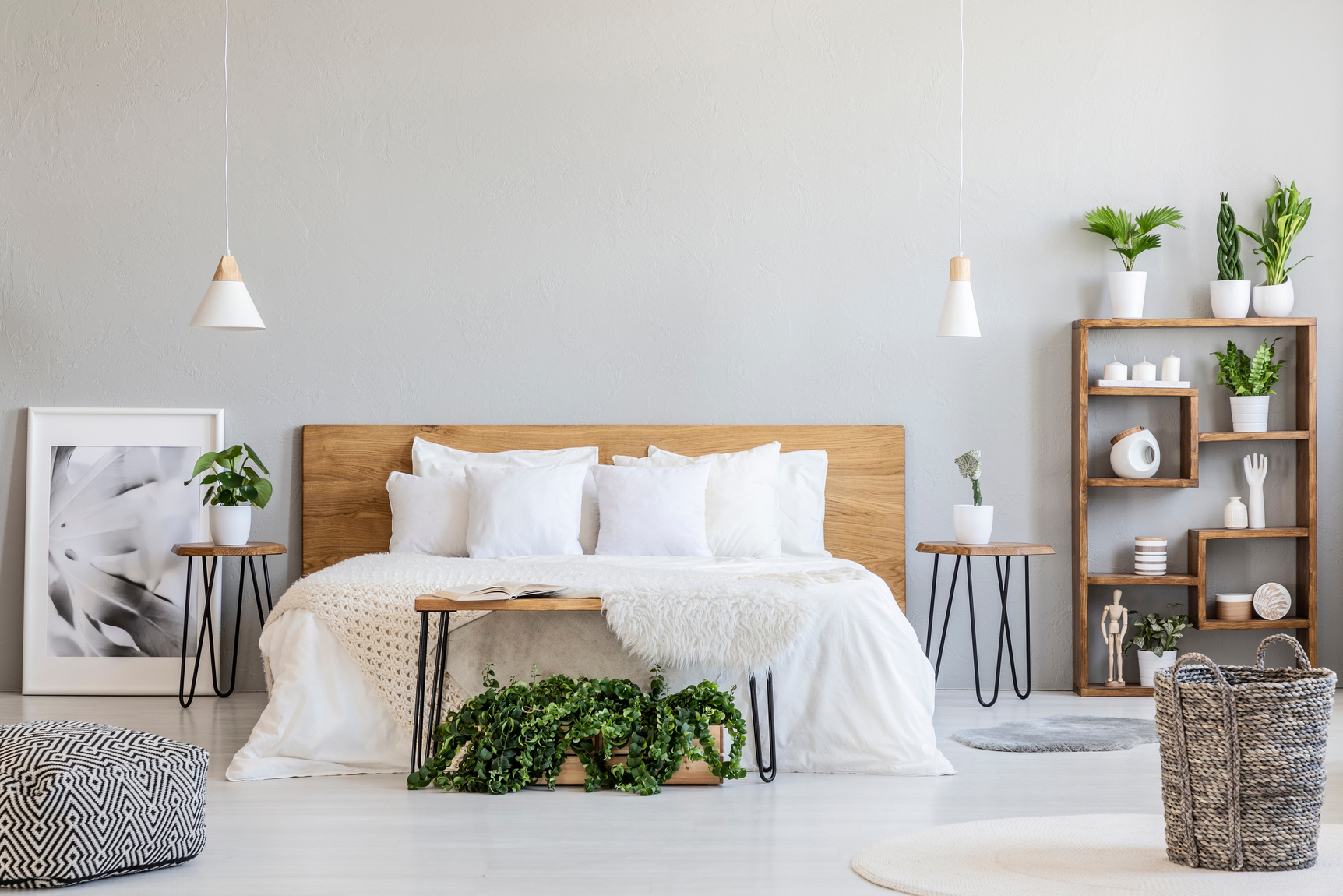 Patterned pouf and basket in bright bedroom interior with lamps, plants and poster next to bed. Real photo